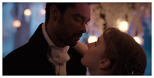 The image is from Bridgerton featuring Simon Basset, the Duke of Hastings, and Daphne Bridgerton. They are dancing closely, looking deeply into each other's eyes in a romantic, candlelit setting. The soft lighting and intimate atmosphere emphasize the romantic tension between the characters during this pivotal scene.