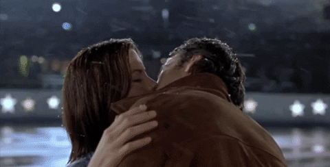 <br>The image shows a romantic moment from the movie Serendipity, where Jonathan, played by John Cusack, and Sara, played by Kate Beckinsale, are kissing passionately in an outdoor setting. Snow is gently falling around them, and they are embracing each other tightly, capturing a tender, magical moment in the film's climax.