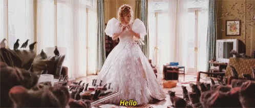 The image shows a scene from the movie Enchanted, where the character Giselle (played by Amy Adams) is standing in a room surrounded by pigeons, rats, and other small animals. She is wearing a large, elegant white gown, and cheerfully says "Hello" to the creatures as they gather around her. This whimsical scene highlights her ability to charm animals, a nod to classic fairytale princess tropes.