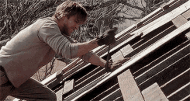 The image shows a scene from The Notebook featuring Ryan Gosling's character, Noah, working on a roof, hammering wooden planks. This moment is part of Noah’s effort to restore the house he promised to build, symbolizing his dedication and love for Allie.